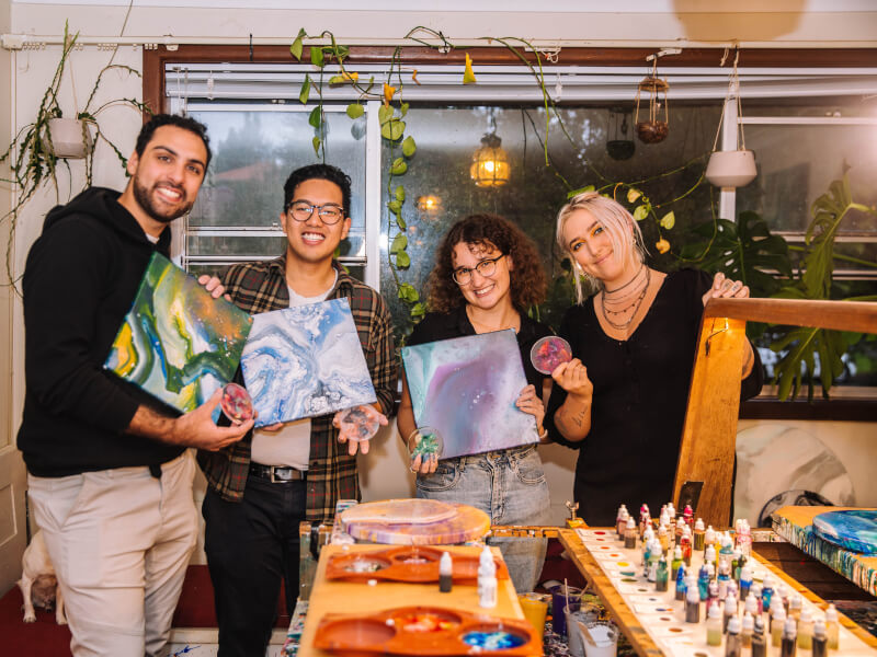 Four smiling people holding up paint canvases.